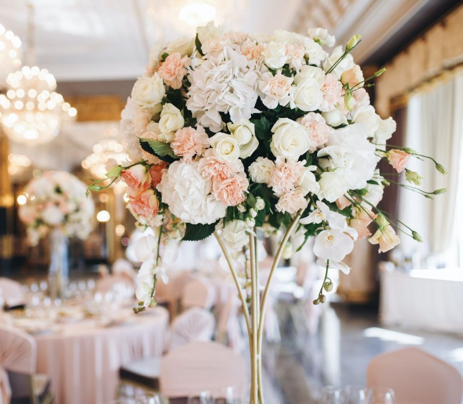 A vase filled with white and pink flowers is on a table at a wedding reception.