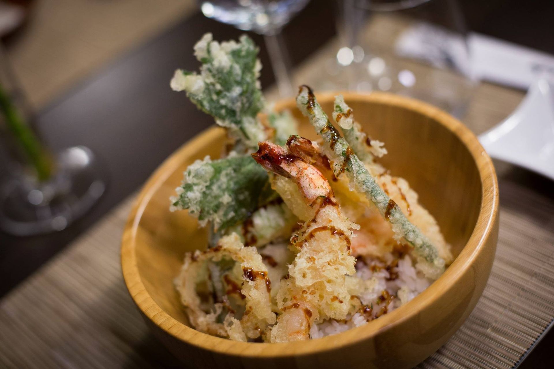 Una ciotola di legno piena di gamberi fritti e verdure su un tavolo.