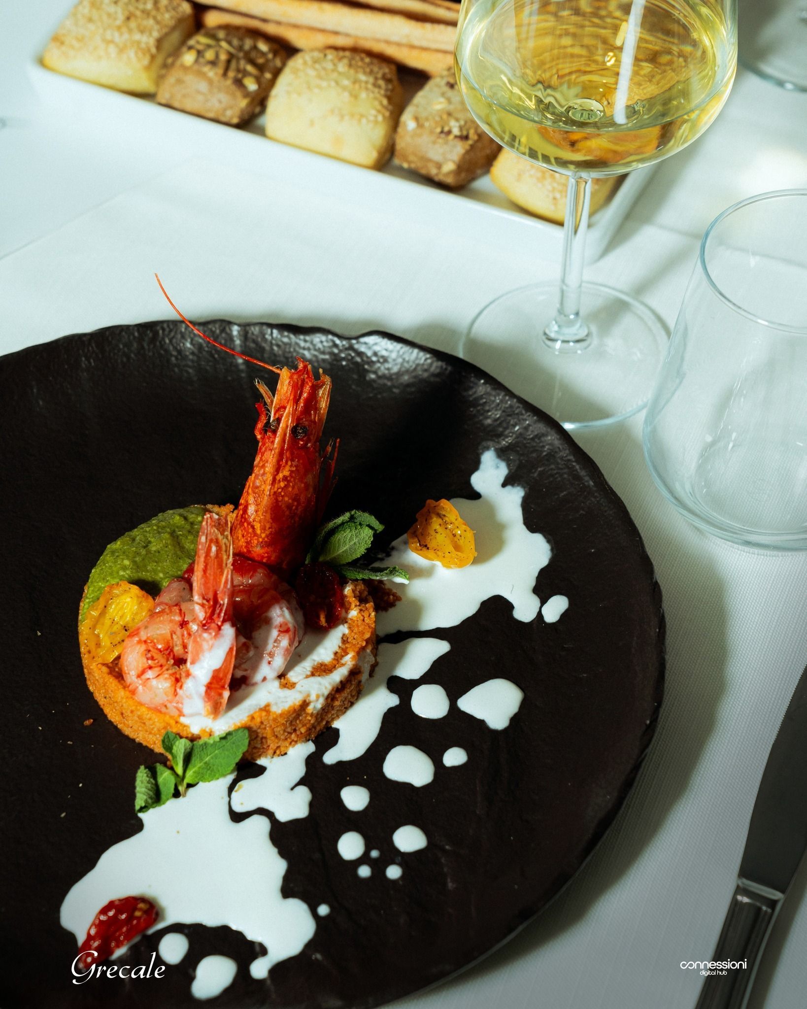 Un piatto di cibo con un gambero sopra accanto a un bicchiere di vino