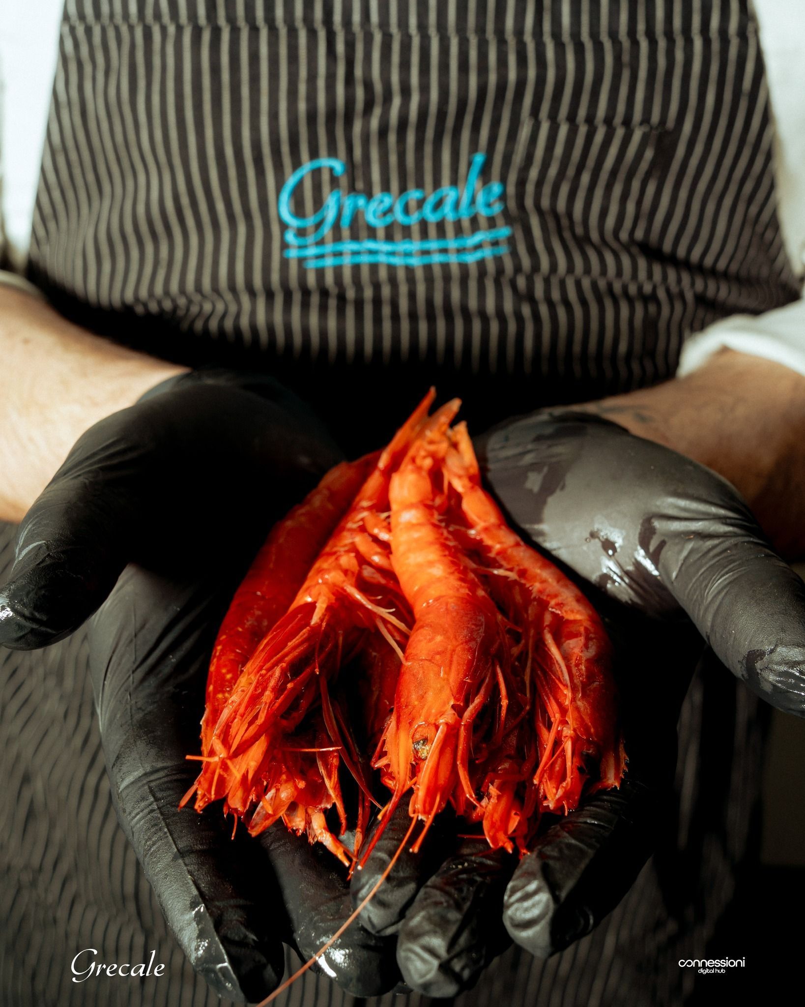 Una persona che indossa guanti neri tiene in mano un mazzo di gamberi rossi