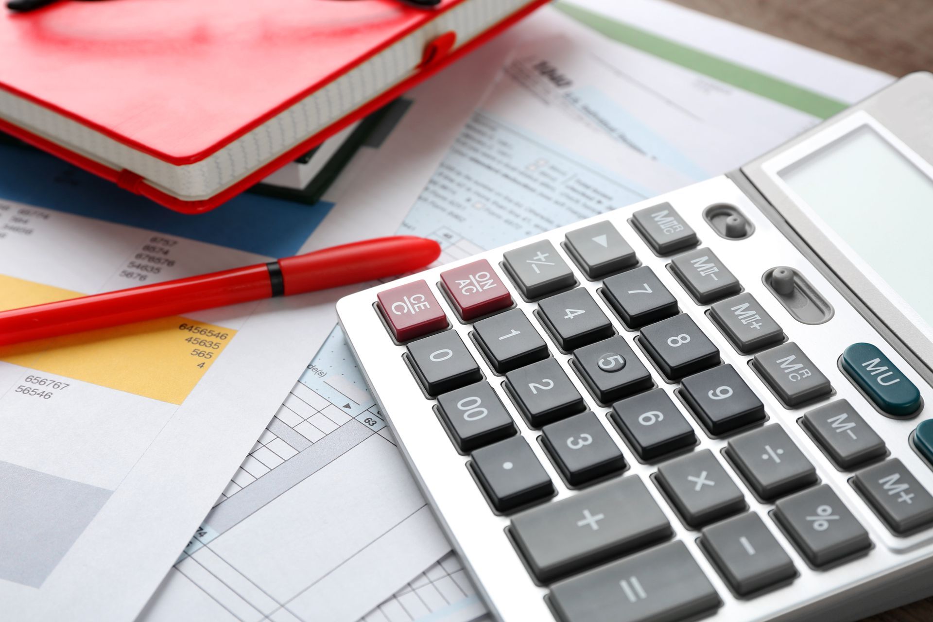 Calculator, red pen, notebook, and documents on a desk, indicating financial calculations.