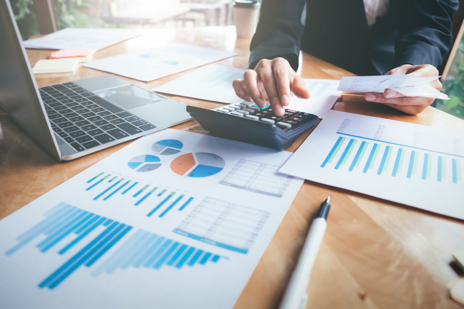 Person using calculator with financial charts and laptop on a desk. Person using calculator with financial charts and laptop on a desk.