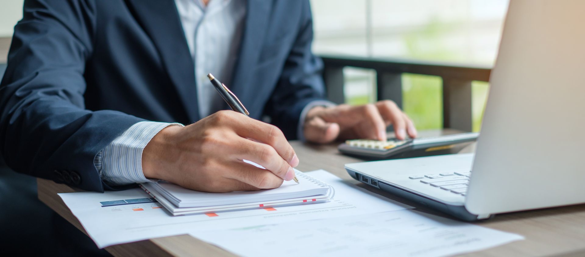 Person in suit writing notes, using a calculator and laptop. Person in suit writing notes, using a calculator and laptop.