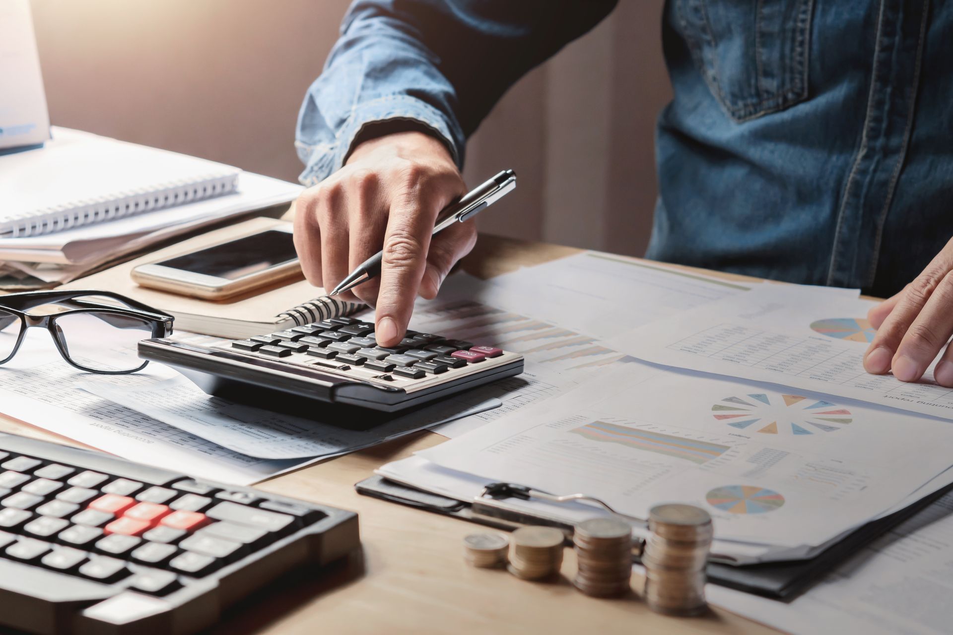 Person using a calculator, looking at financial documents, with stacked coins.