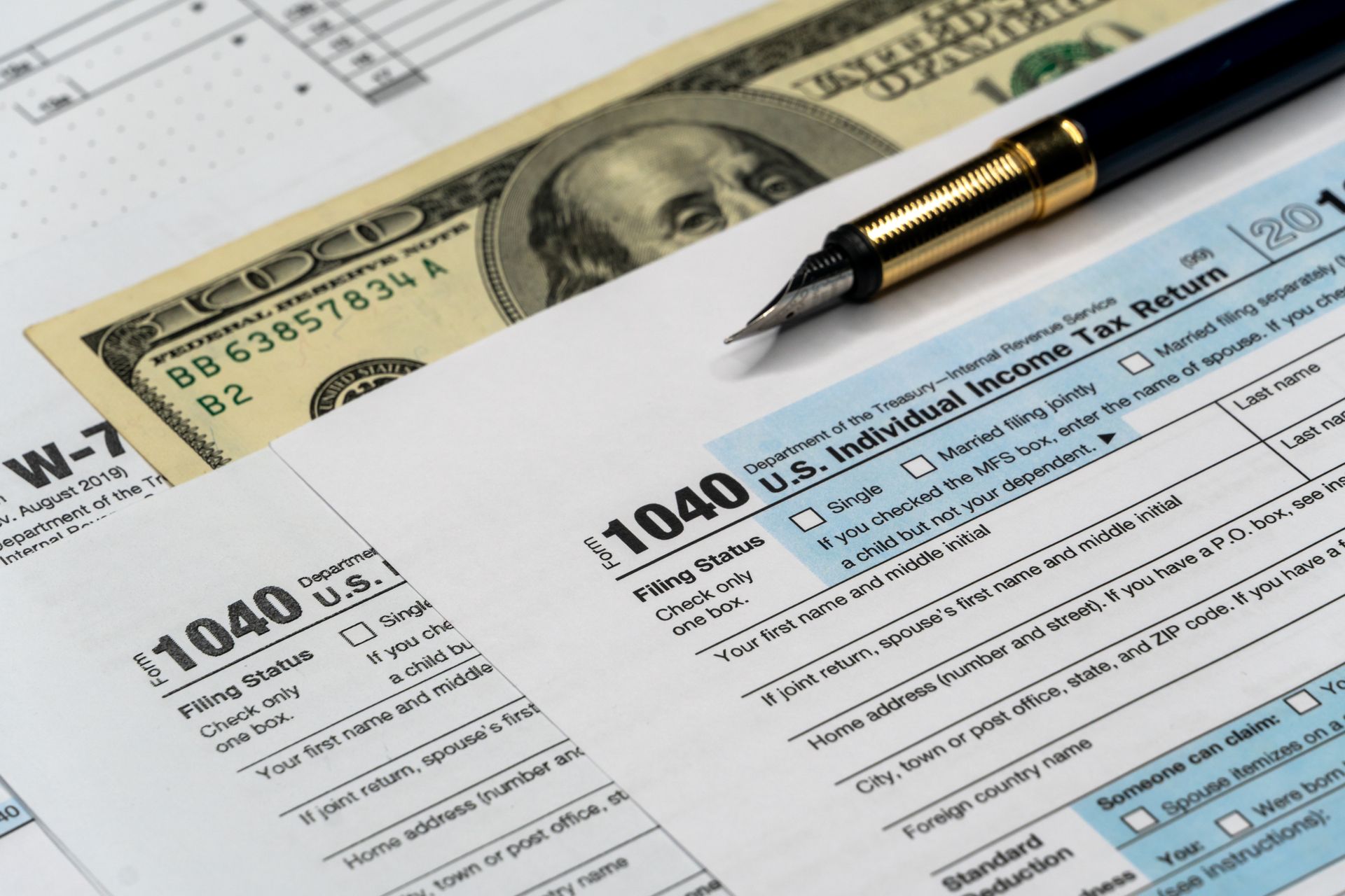 Tax forms, pen, and US currency on a table.