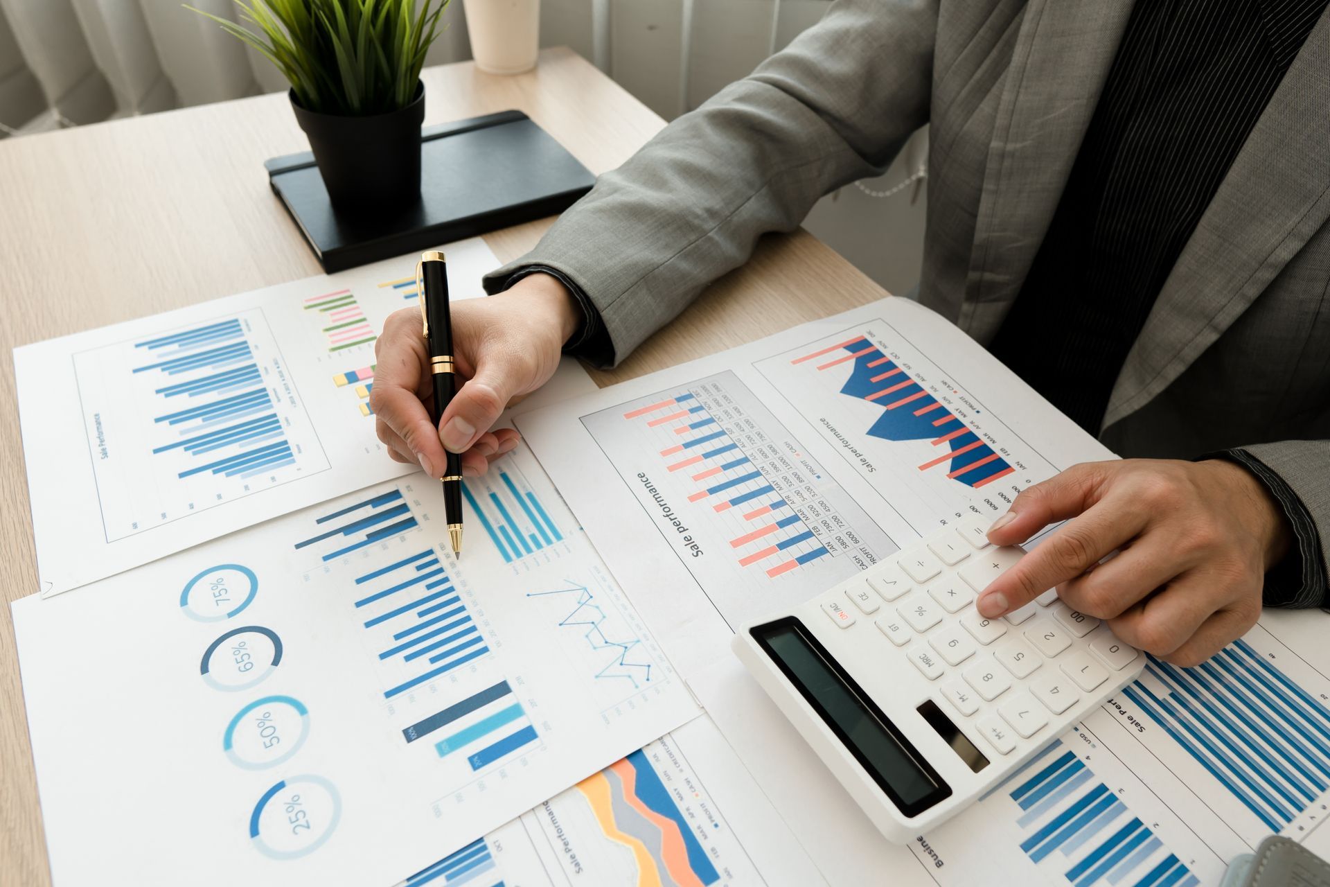 Person in suit jacket reviews charts and uses calculator at a desk. Person in suit jacket reviews charts and uses calculator at a desk.