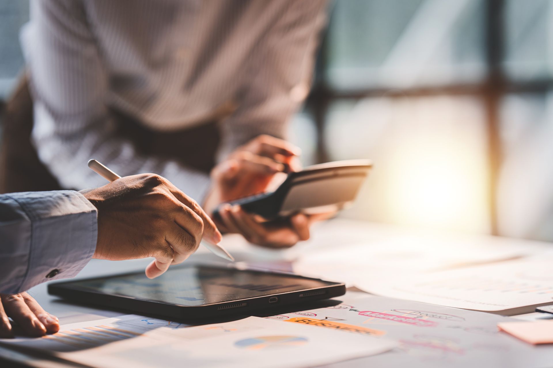 Hands using a calculator and writing on paper with a pen, reviewing financial data on a table. Hands using a calculator and writing on paper with a pen, reviewing financial data on a table.