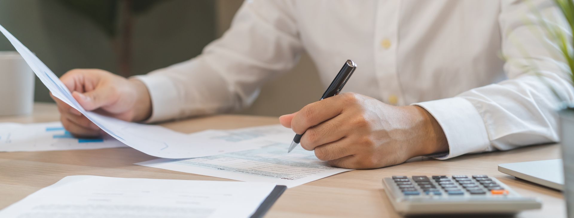 Person in white shirt writing on paperwork at a desk, calculator in view.
