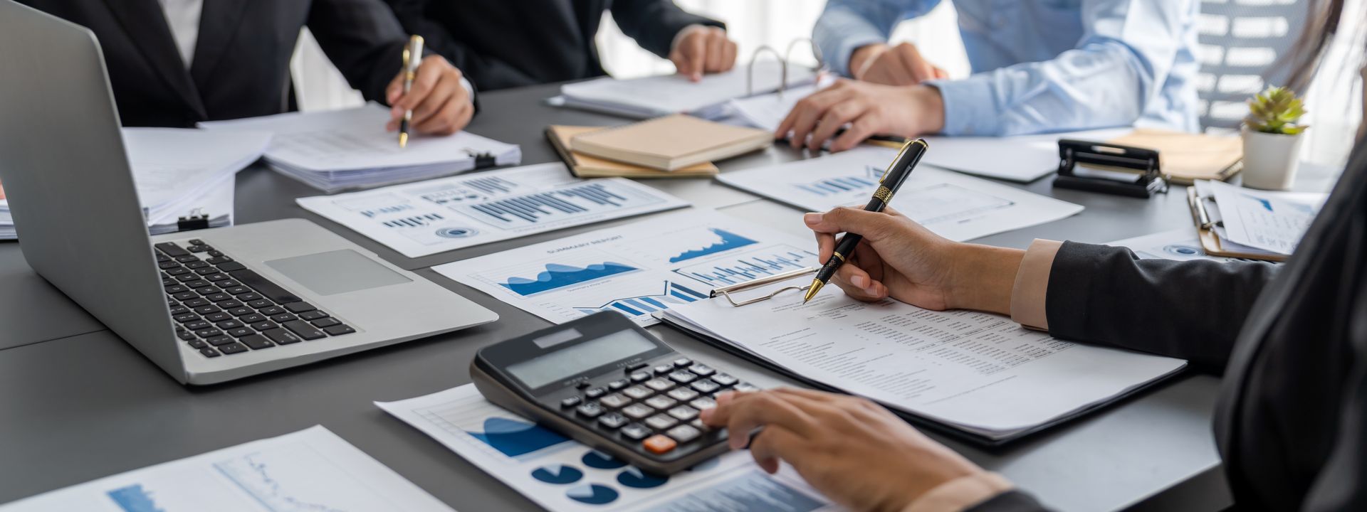 People working on papers and charts at a table with a laptop and calculator.
