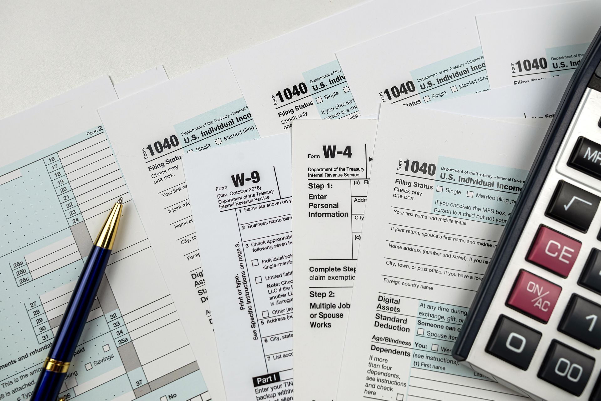 Tax forms, pen, and calculator on white paper.