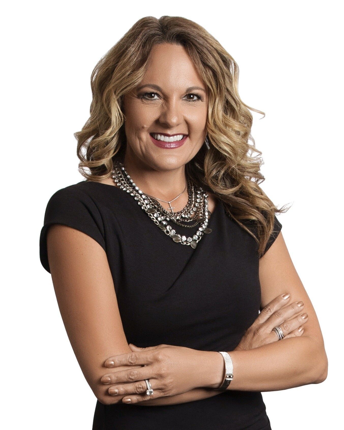 A woman in a black dress and silver necklace is smiling with her arms crossed.