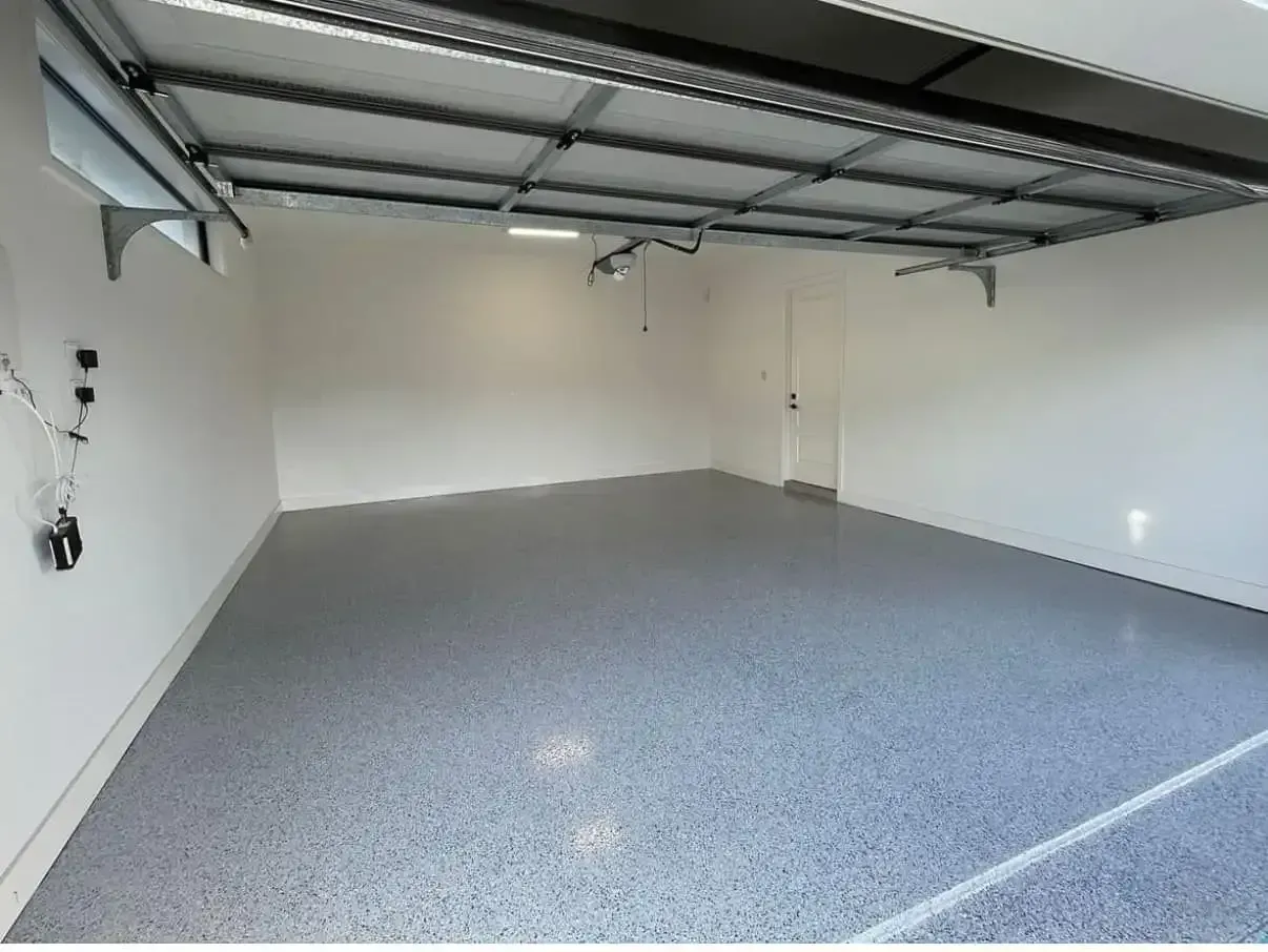 Empty garage with gray speckled floor, white walls, and open ceiling tracks — All Grind & Coat in Atherton, QLD