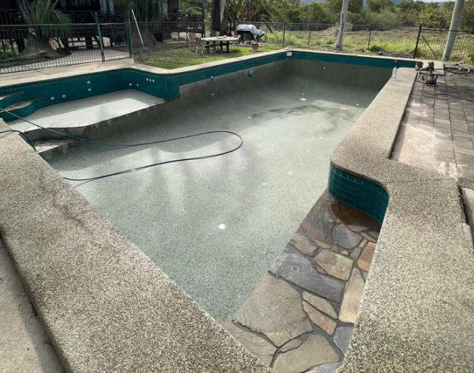 Empty pool with a mottled gray interior, green tiles, and stone edging — All Grind & Coat in Atherton, QLD