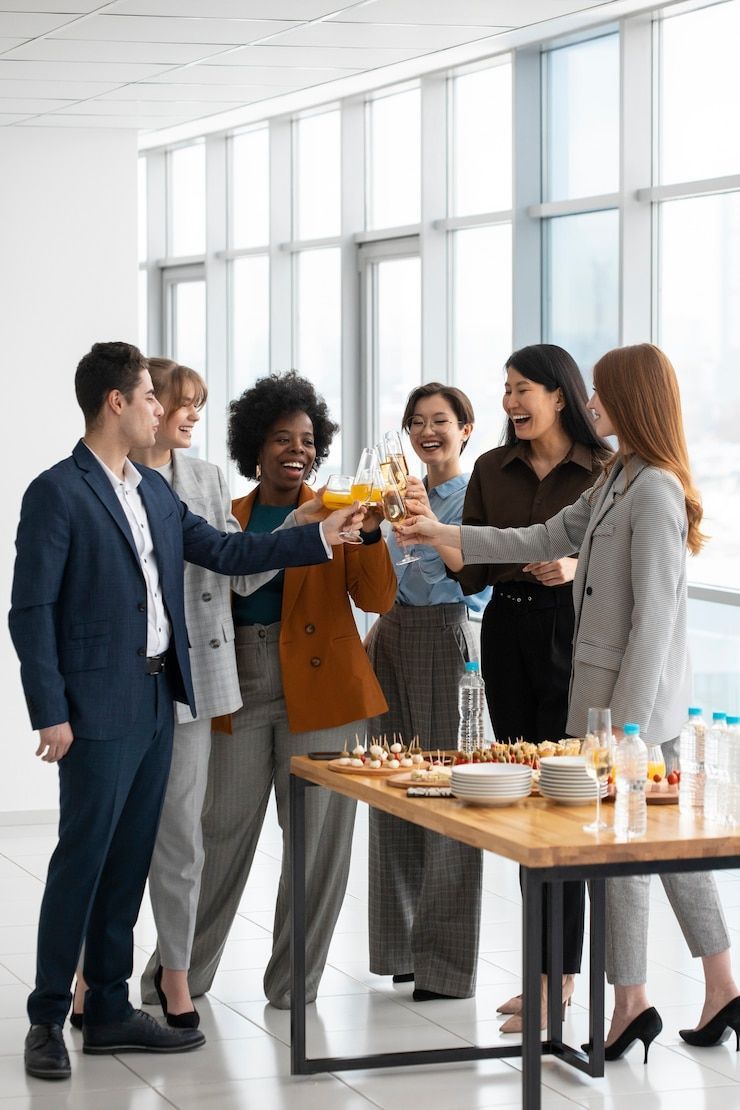 Group of coworkers toasting champagne near a table with food. Office setting, smiles, business attire.