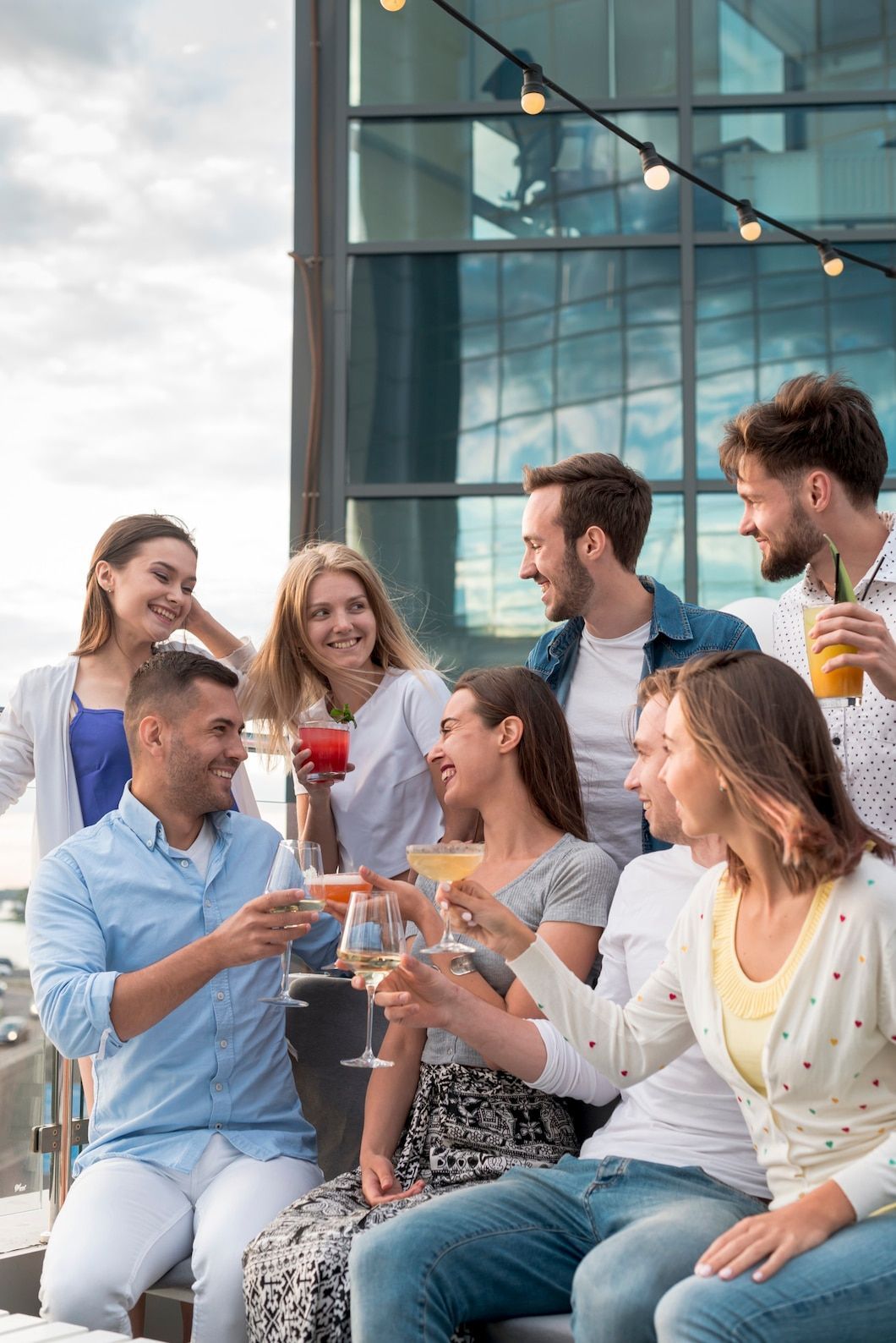 Group of friends toasting drinks on a rooftop. Smiling faces, sunny day, casual attire.