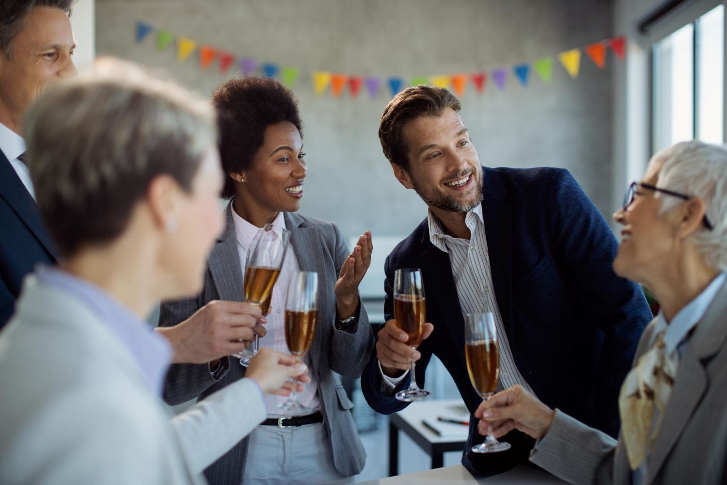 Office workers clinking champagne flutes in a celebratory toast. Colorful banner in background.