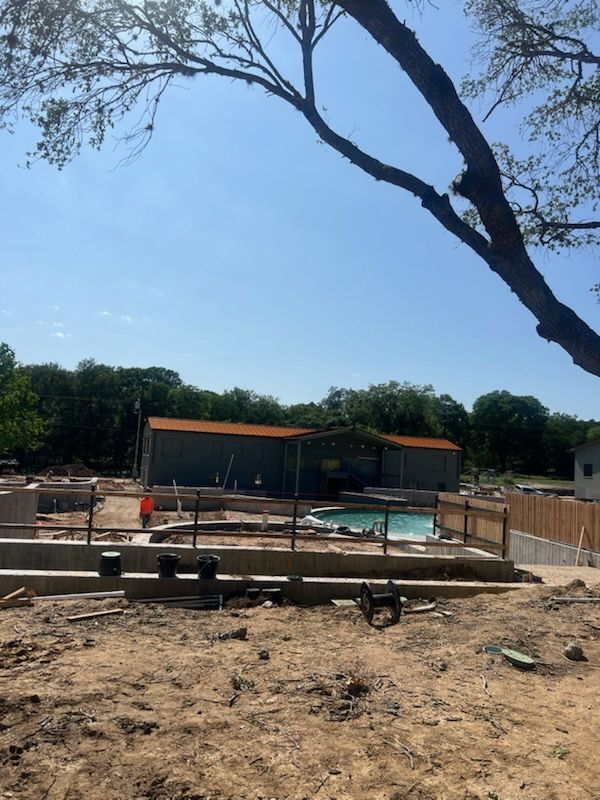 Construction site with a pool, building, and tree branches under a clear blue sky.