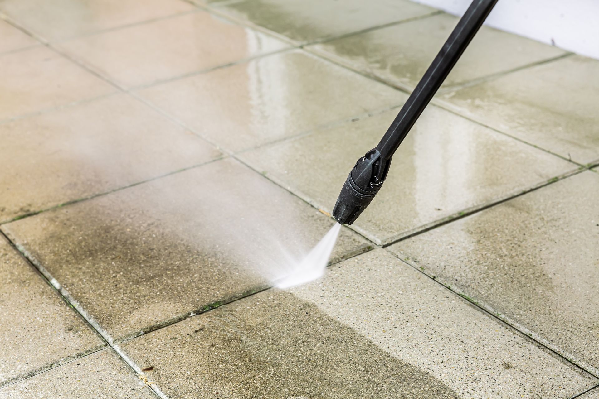 Pressure washer spraying water onto a dirty, tiled surface; cleaning.