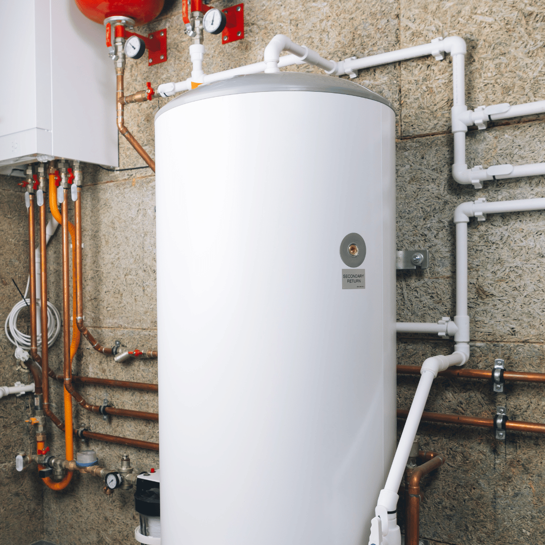 A white water heater is sitting in a room with pipes.