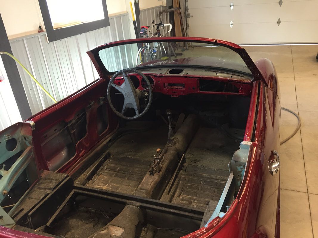 A red convertible car is sitting in a garage.