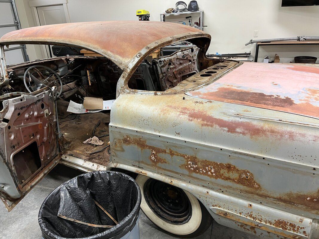 An old rusty 1958 Buick Roadmaster  is sitting in a garage with the door open.
