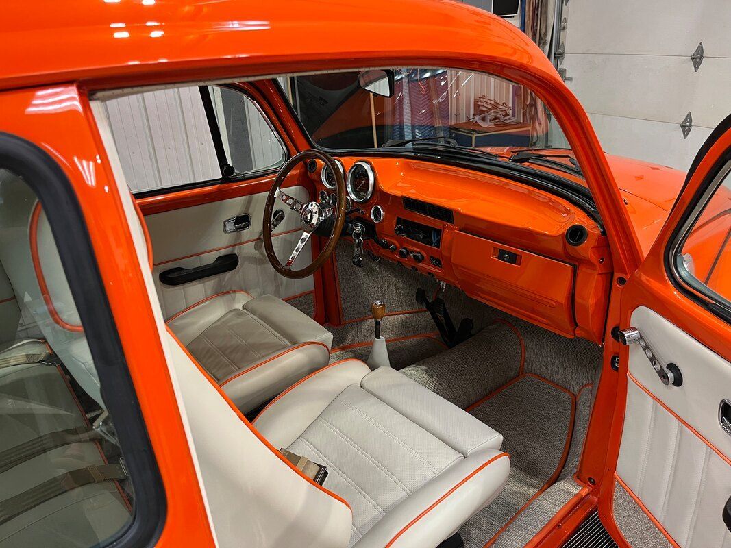 The interior of an orange car with white seats and a wooden steering wheel.