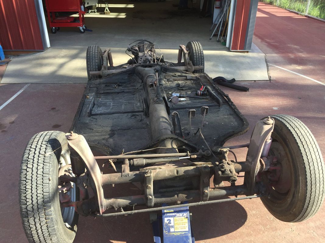A car chassis is sitting on a jack in front of a garage.