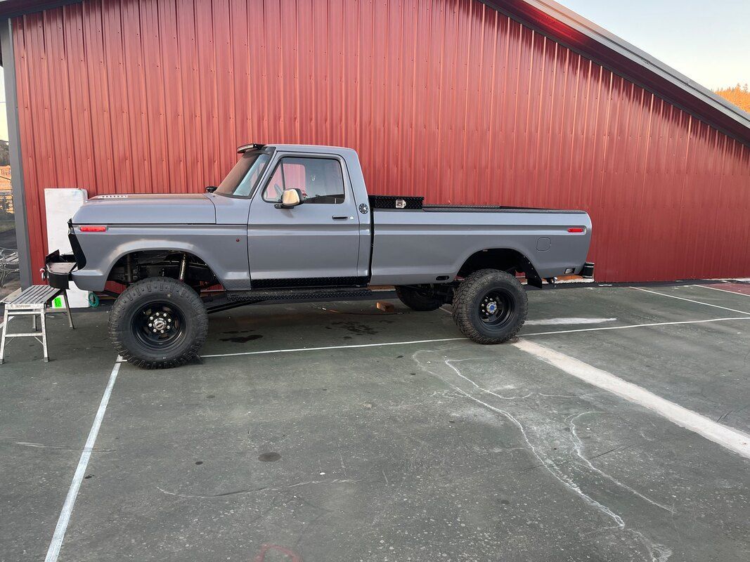 A gray truck is parked in a parking lot in front of a red barn.