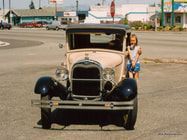 A woman is standing next to an old car on the side of the road.