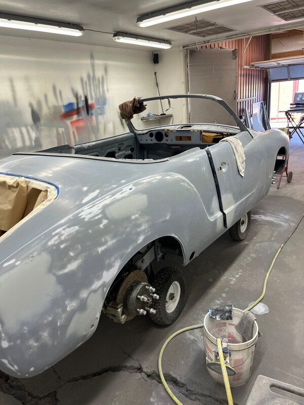 A convertible car is being painted in a garage.