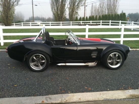 A black sports car is parked in front of a white fence