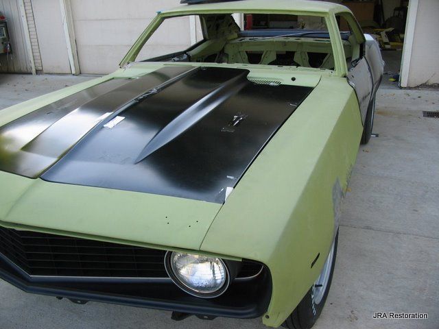 A green car with a black hood is parked in a garage