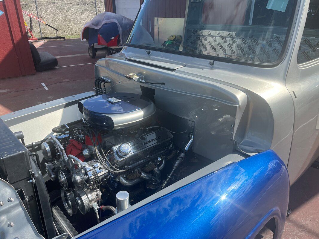 A silver truck with the hood open and a blue fender.