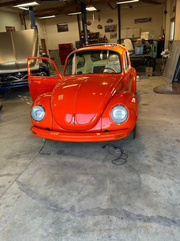 A red beetle is parked in a garage with its doors open.