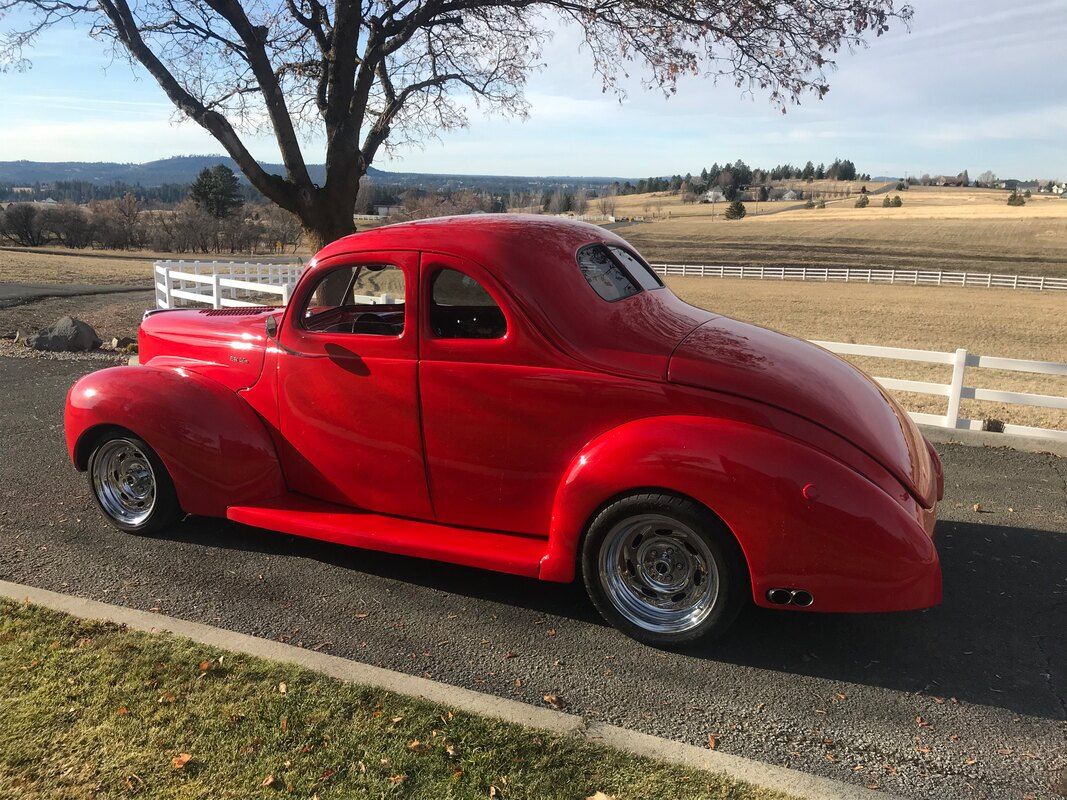 A red car is parked on the side of the road next to a tree.