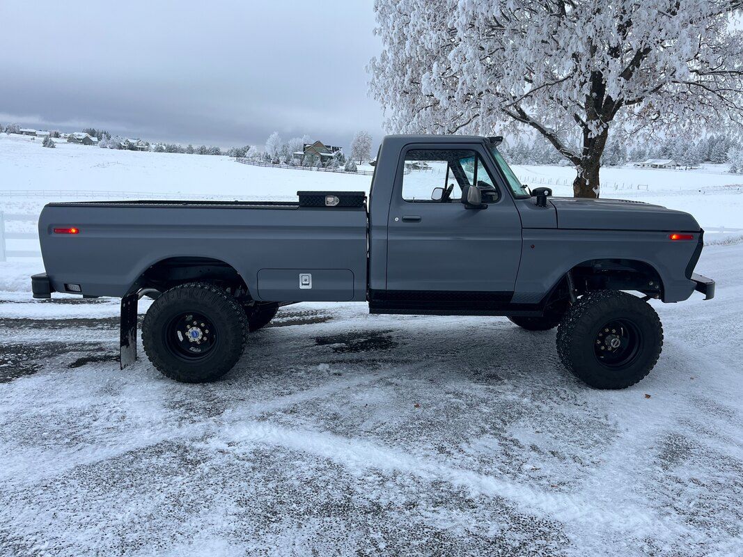 A gray truck is parked in the snow in a parking lot.