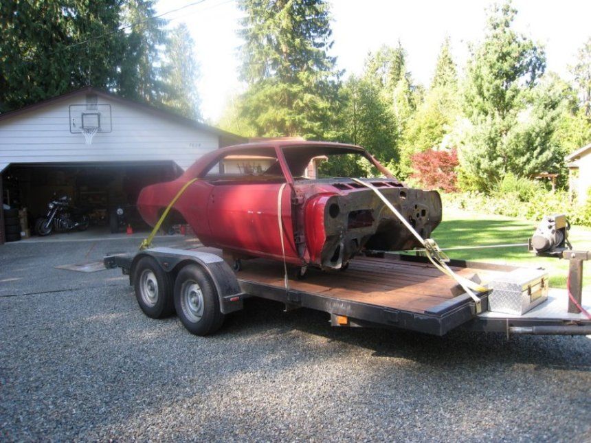 A red car is on a trailer in front of a garage