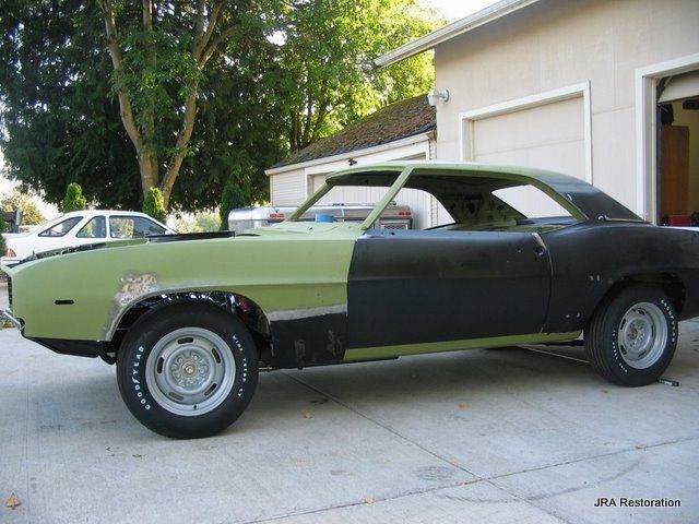A green and black car is parked in front of a garage
