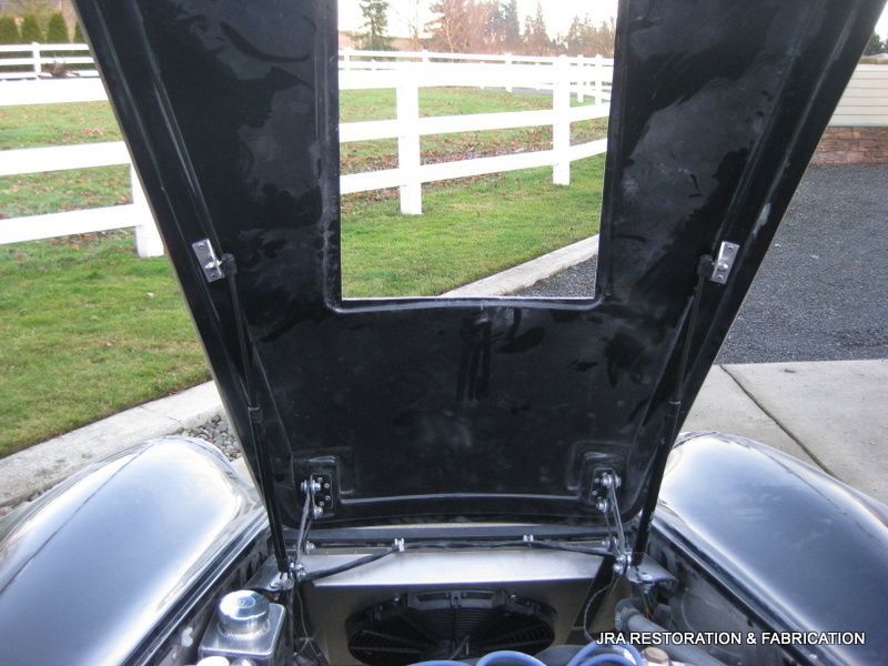 The hood of a black car is open with a white fence in the background