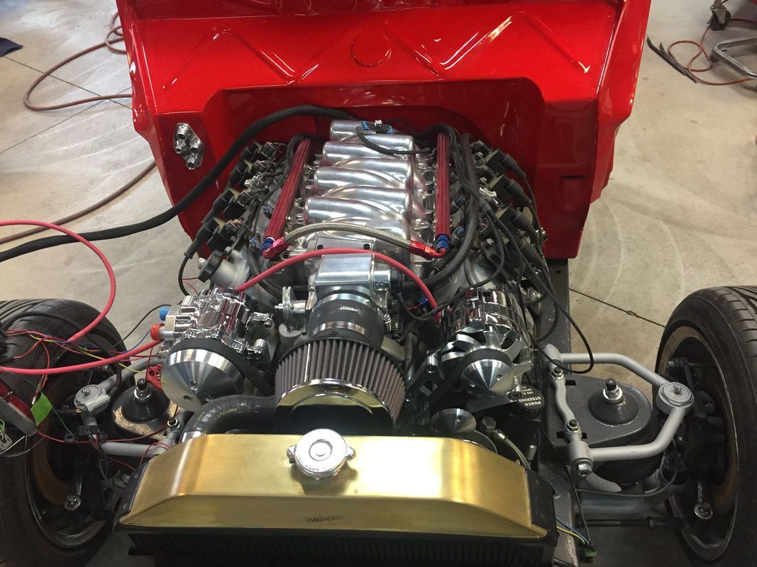The engine of a red car is being worked on in a garage.