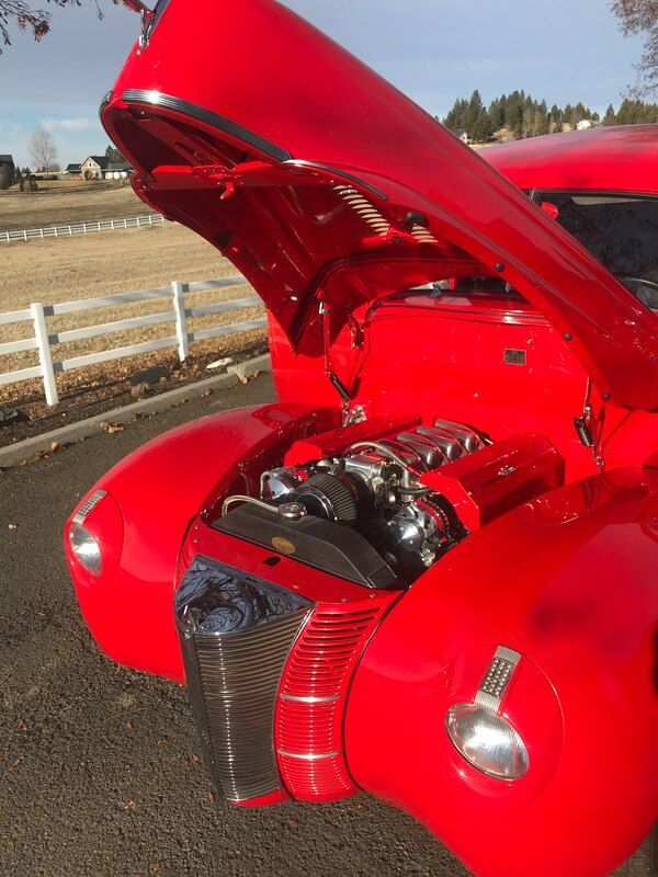 A red car with the hood up is parked on the side of the road.