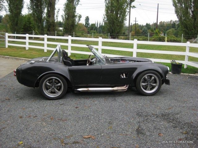 A black sports car is parked in front of a white fence
