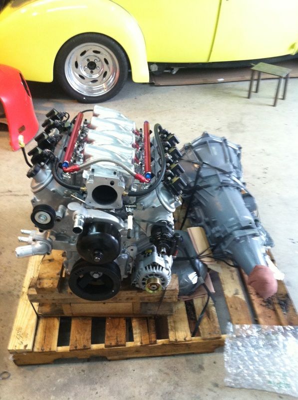 A car engine is sitting on a wooden pallet next to a yellow car