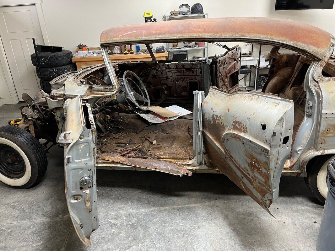 An old rusty 1958 Buick Roadmaster  is sitting in a garage with its doors open.