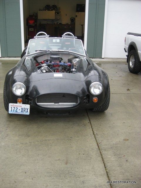 A black sports car with the hood up is parked in front of a garage.