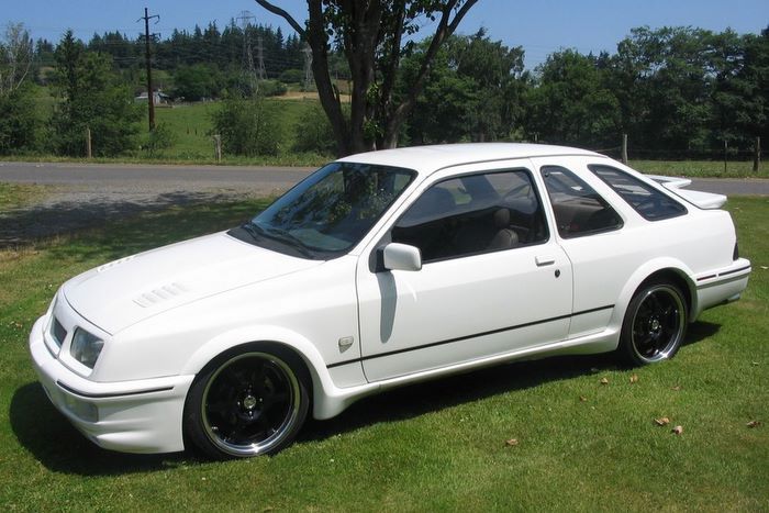 A white car with black wheels is parked in the grass