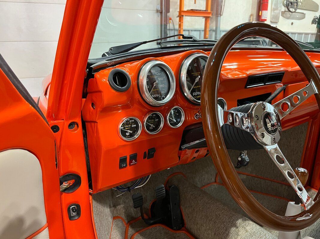 A close up of the dashboard of an orange car with a wooden steering wheel.