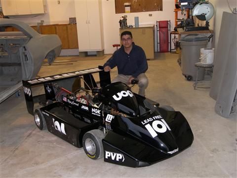 A man sits next to a go kart that says 101 on it