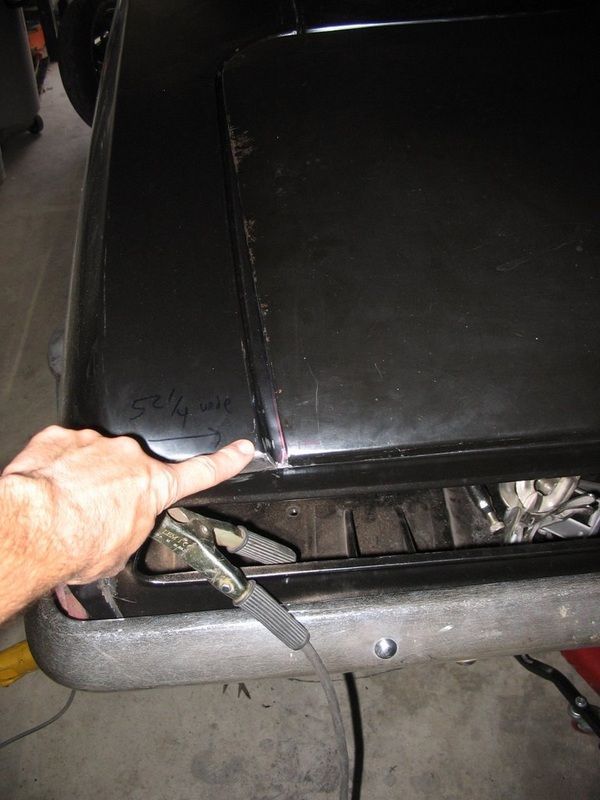 A person is pointing at the hood of a black car.