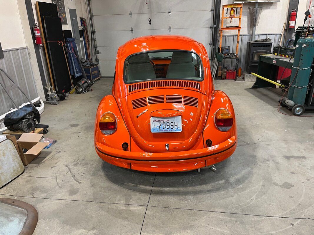 A bright orange beetle is parked in a garage.
